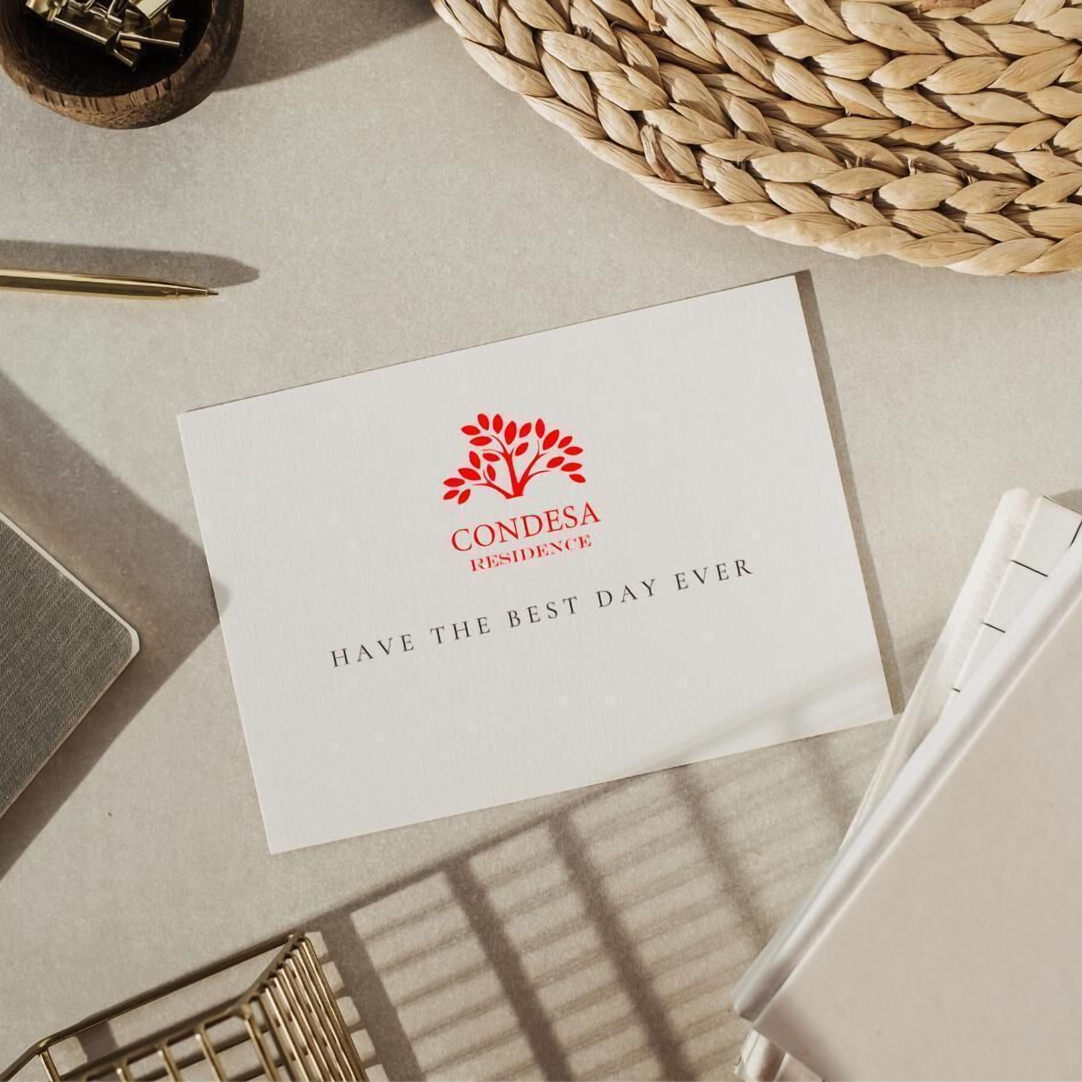 A white card with a logo and text "CONDESA RESIDENCE" and "HAVE THE BEST DAY EVER" on a table.