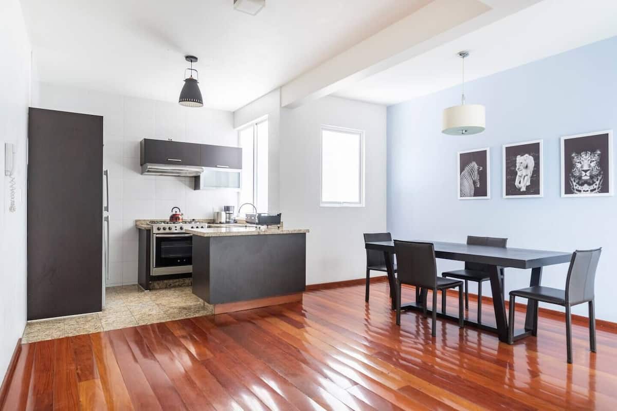Een moderne keuken met een centraal eiland, een zithoek met een tafel en stoelen, en een groot raam dat zorgt voor veel daglicht.