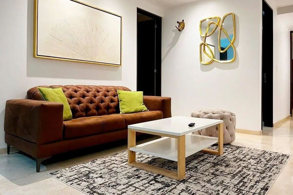 Een moderne woonkamer met een bruine leren bank, een witte salontafel en een vloerkleed met een patroon.