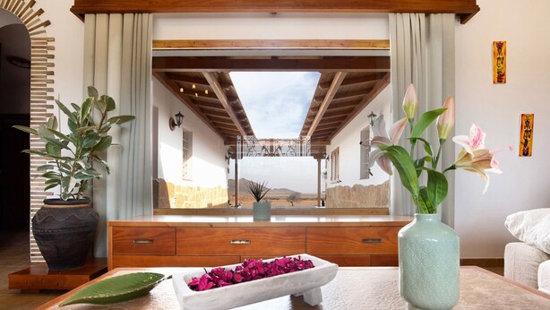 A room with a large window, wooden beams, a white console table, a vase with flowers, and a potted plant. - Vacation Home 'Casa Glory' with Mountain View, Wi-Fi and Air Conditioning (Antigua)
