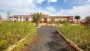 A two-story house with a gravel pathway leading to the entrance, surrounded by greenery and a clear sky. - Vacation Home 'Casa Glory' with Mountain View, Wi-Fi and Air Conditioning (Antigua)