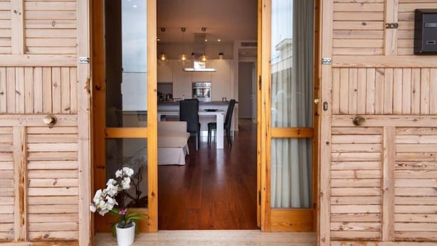 A wooden-framed doorway leading to a modern kitchen and dining area with a potted plant.