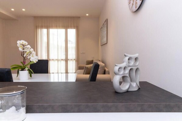 A modern living room with a dining table, a sofa, a decorative vase, and a clock on the wall.