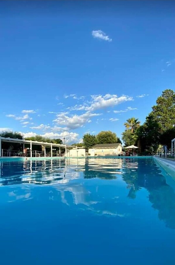 Un ciel bleu clair avec quelques nuages, une piscine et quelques arbres en arrière-plan.