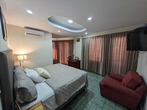 Une chambre d’hôtel équipée d’un lit, d’un bureau, d’une chaise, d’une télévision et d’un luminaire au plafond.