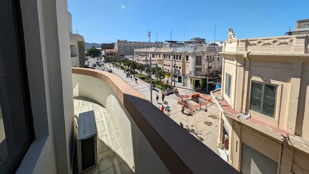 Een balkon met uitzicht op een stadstraat, gebouwen en een heldere lucht.