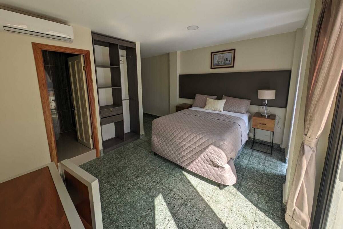 Een hotelkamer met een bed, een nachtkastje, een aan de muur bevestigde televisie en een deur naar een andere kamer.