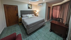 Een hotelkamer met een bed, een bureau, een stoel, een deur, een airconditioning en een schilderij aan de muur.