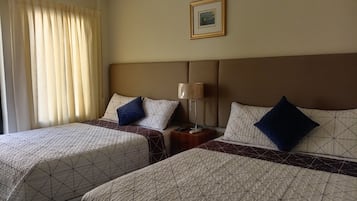 Quarto de hotel com duas camas, uma mesa de cabeceira com abajur e um quadro na parede.