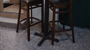 Un coin repas avec une table ronde et deux chaises, un vase de fleurs et un rideau foncé.