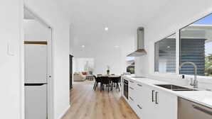 Una cocina moderna con armarios blancos, un ventanal grande y una zona de comedor con mesa y sillas.