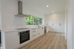 A modern kitchen with white cabinetry, a stainless steel range hood, and a window providing a view of greenery. - Epic Escape - Swim Spa, Redwoods, Sleeps 8 (Rotorua)