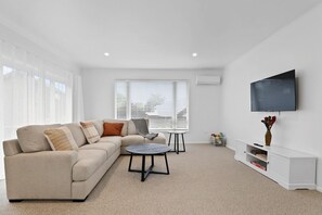 A modern living room with a sofa, coffee table, and a flat-screen TV mounted on the wall. - Epic Escape - Swim Spa, Redwoods, Sleeps 8 (Rotorua)