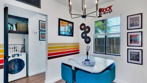 Una cocina moderna con lavadora integrada, un comedor con sillas azules y una pared decorada con discos de vinilo y un letrero que dice 'ROCK'.