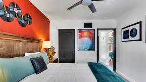 Habitación de hotel con cama, ventilador de techo, pared decorada con discos de vinilo, puerta y obras de arte enmarcadas.