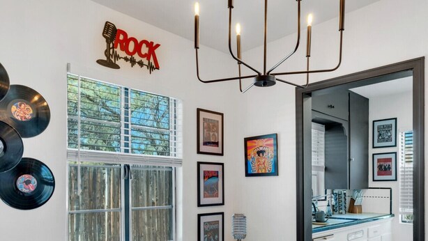 Un comedor con una mesa blanca, sillas color turquesa y un candelabro. Hay discos de vinilo en la pared y cuadros enmarcados.