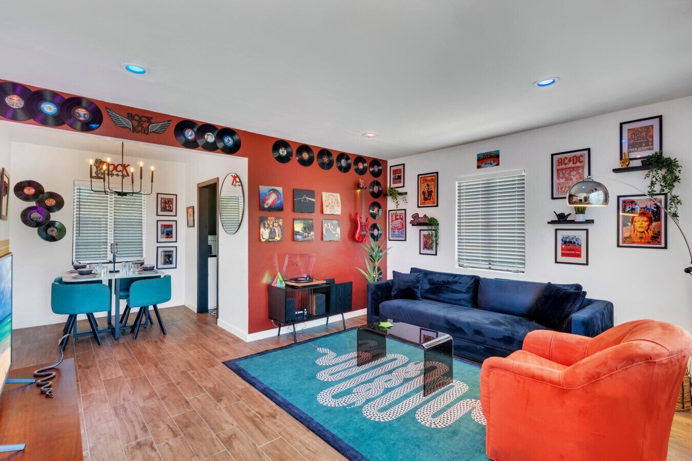 Uma sala moderna com um sofá azul, uma poltrona laranja e uma área de jantar com mesa e cadeiras azuis.