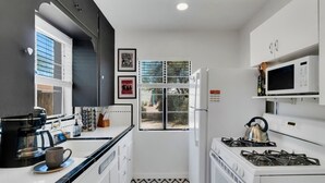 Cocina compacta con armarios blancos, estufa a gas, microondas y cafetera.