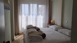 Ein Hotelzimmer mit einem Bett, einer Nachttischlampe, einem Deckenventilator und Blick auf Gebäude durch transparente Vorhänge.