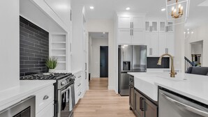 Eine moderne Küche mit weißen Schränken, einer schwarzen Küchenrückwand, Edelstahlgeräten und Holzboden.