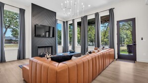 Ein modernes Wohnzimmer mit einer langen Ledersofa, einem Kamin, einem Flachbildfernseher und großen Fenstern mit Blick ins Freie.