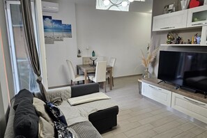 Een woonkamer met een bank, televisie, eethoek en een raam met gordijnen.