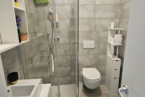 Een moderne badkamer met een douchecabine van glas, een wit toilet en een inbouwplankje met toiletartikelen.