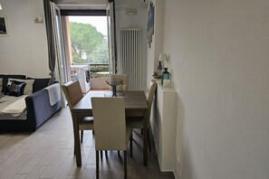 Een woonkamer met een bank, een eettafel met stoelen, een radiator en een raam met gordijnen.