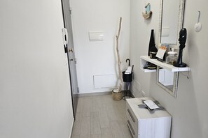 En hall med en vit dörr, en spegel, en hylla med diverse föremål och en liten växt.