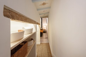A narrow hallway with shelves holding baskets and a lamp in the background.