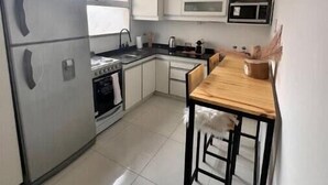 Una cocina compacta equipada con refrigerador, estufa, microondas y un comedor de madera con dos sillas.