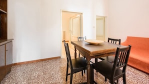 Un comedor con una mesa de madera, cuatro sillas, un centro de mesa redondo, un sofá y un armario.