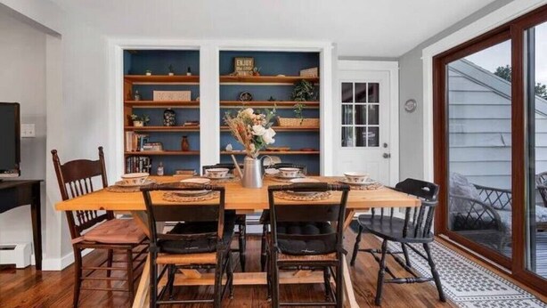 Un comedor con una mesa y sillas de madera, rodeado de estanterías empotradas con objetos decorativos y libros.