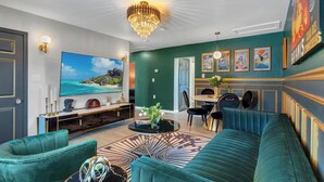 Een moderne woonkamer met een grote televisie, smaragdgroene banken, een kroonluchter en kunst aan de muren.