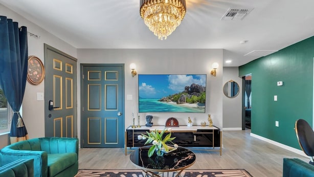 Een moderne woonkamer met smaragdgroene meubels, een grote televisie en een decoratieve kroonluchter.
