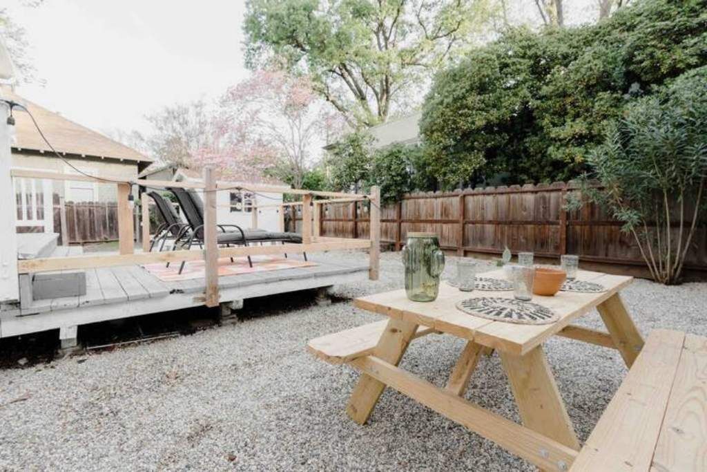 Une terrasse en bois avec une table et des chaises, entourée d’une clôture en bois et de verdure.