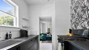 A modern kitchen with a black countertop, a coffee machine, and a stove. There is a window providing natural light and a view of a living area with a blue sofa. - Fox at Fourth Street Walk to downtown Chico (Chico)
