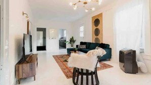 A spacious living room with a modern chandelier, a green sofa, a white furry chair, and a flat-screen TV on a wooden stand. - Fox at Fourth Street Walk to downtown Chico (Chico)