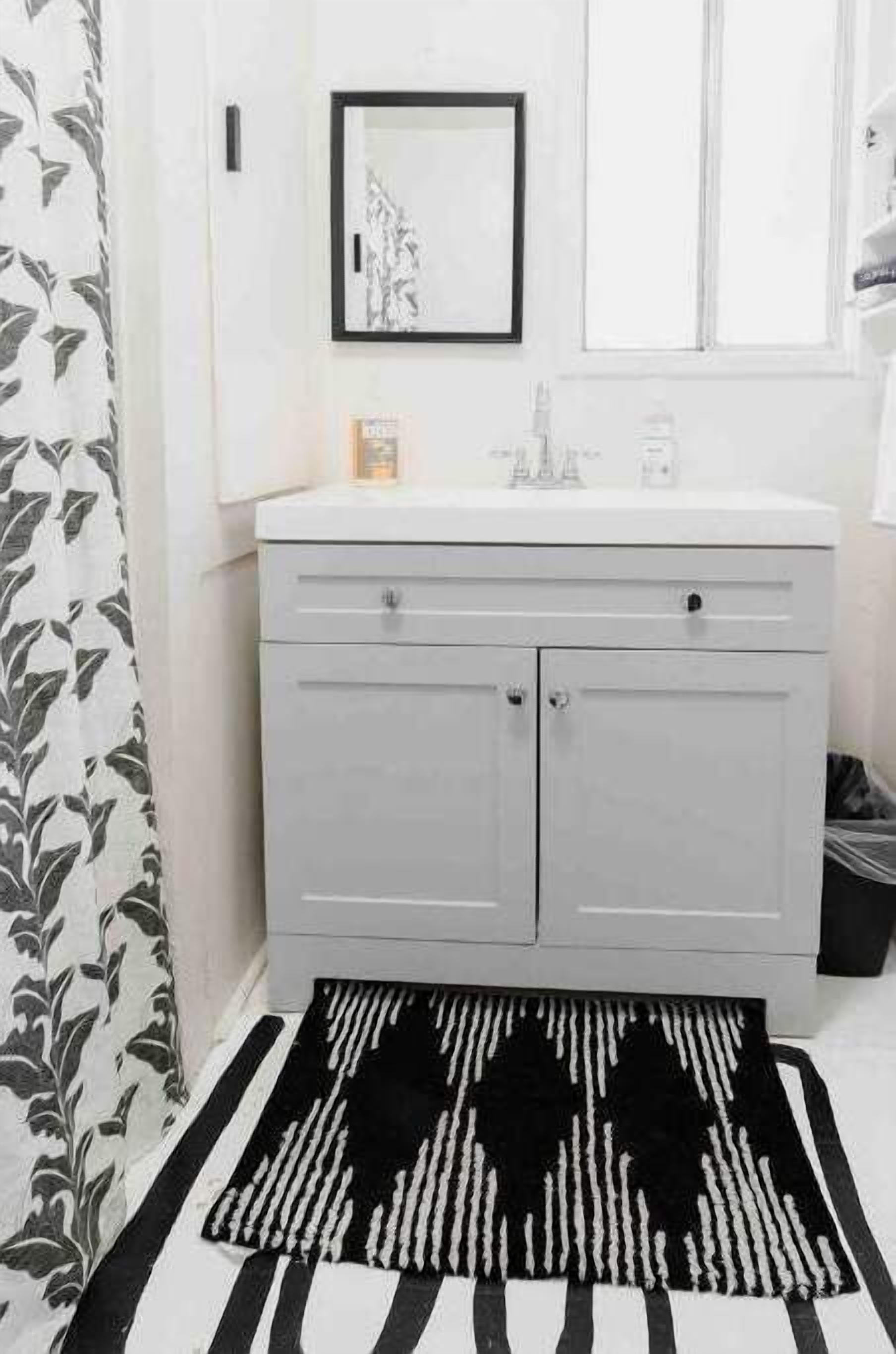 Une salle de bain avec un meuble-lavabo blanc, un tapis noir et blanc et un tableau encadré au mur.