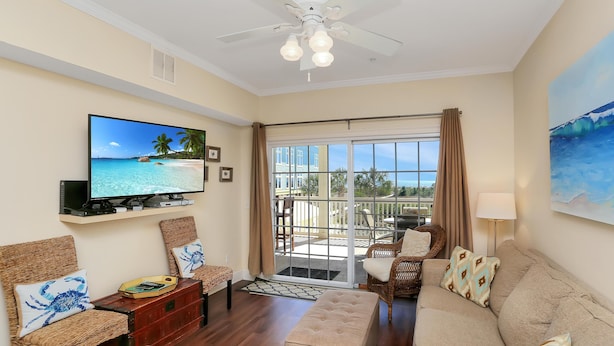 A living room with a TV, wicker furniture, a sofa, and a balcony with a view. - Dunes Club 1B (Port St. Joe)