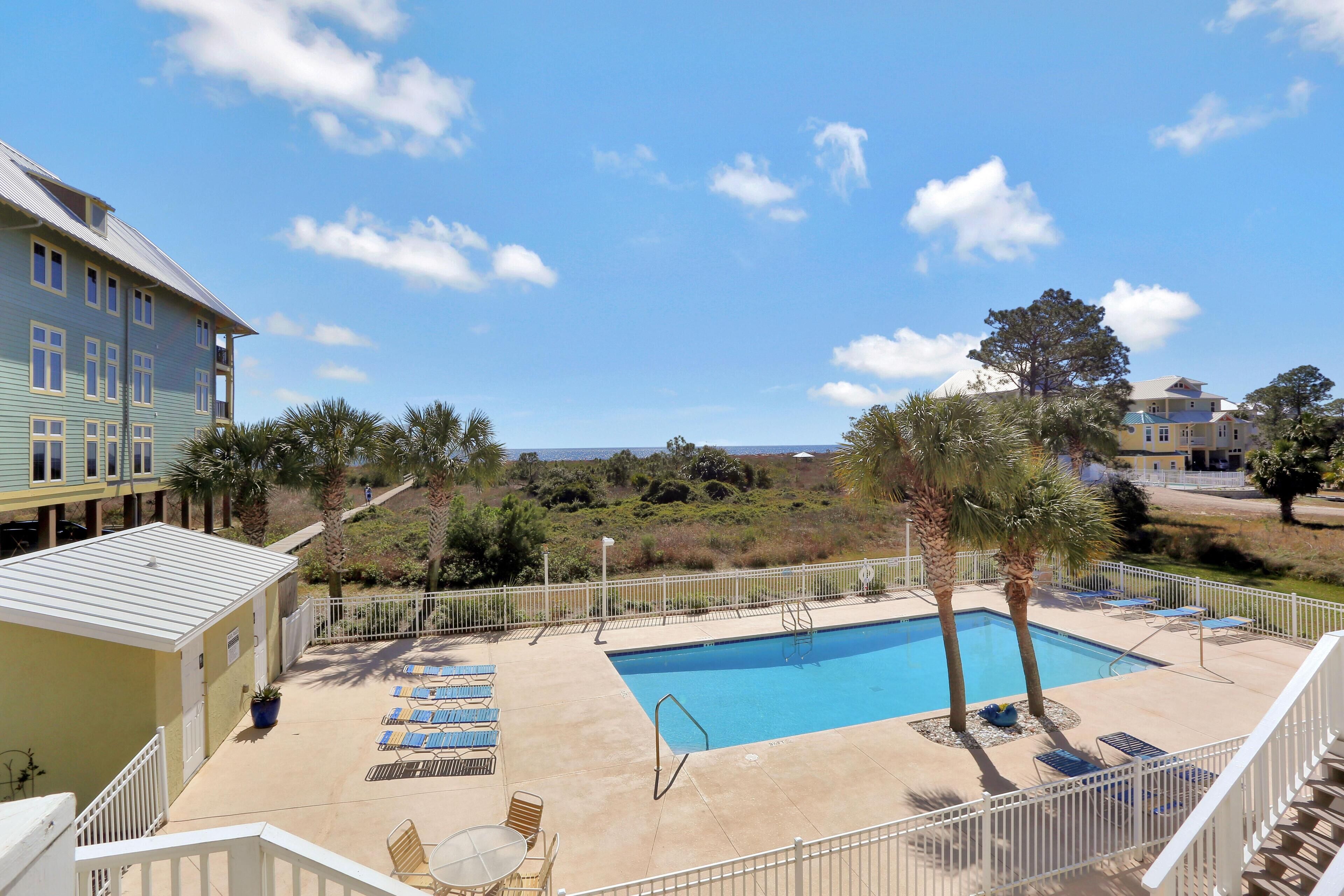 A pool area with lounge chairs, a small table, and a view of the ocean.