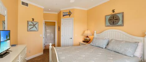 A bedroom with a bed, a television, a ceiling fan, and a door leading to another room.