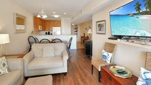 A living room with a sofa, chairs, a television, and a dining area with a table and chairs. - Dunes Club 1B (Port St. Joe)