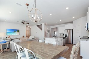 Enjoy meals at the central dining table with white chairs, surrounded by a well-lit kitchen with a central island and sink.