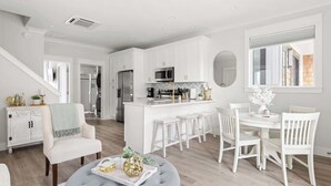 Una cocina moderna con armarios blancos, una isla central y un comedor con sillas y una mesa blancos.