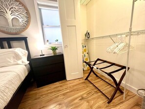 Quarto com cama, mesa de cabeceira, varal de roupa e janela com vista.