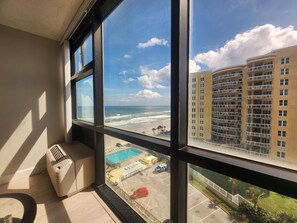 Una habitación con un ventanal grande que da a una playa, una piscina y un estacionamiento.