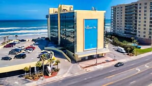 Een modern gebouw met een blauwe deur, naast een parkeerplaats met meerdere auto's, met uitzicht op een strand.