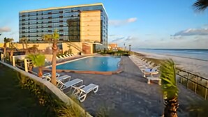 Een modern hotel met een zwembad, ligbedden en uitzicht op het strand.