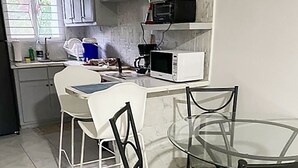 A compact kitchen with white cabinets, a microwave, a coffee maker, and a glass dining table with chairs. - Charming tropical beach retreat Suite 1 (Hellshire)